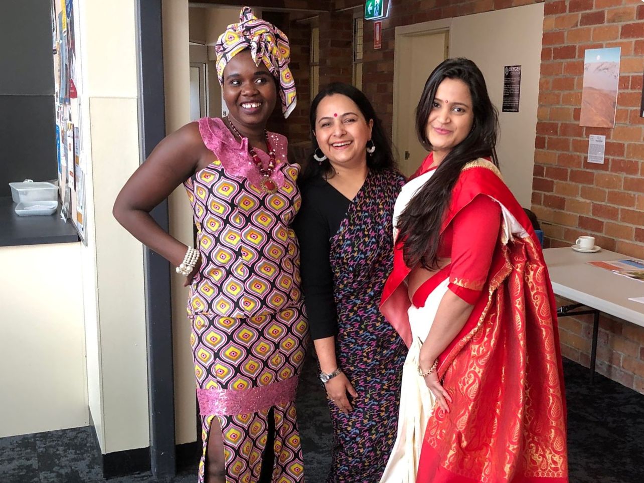 Three women in colourful cultural attire smiling together.