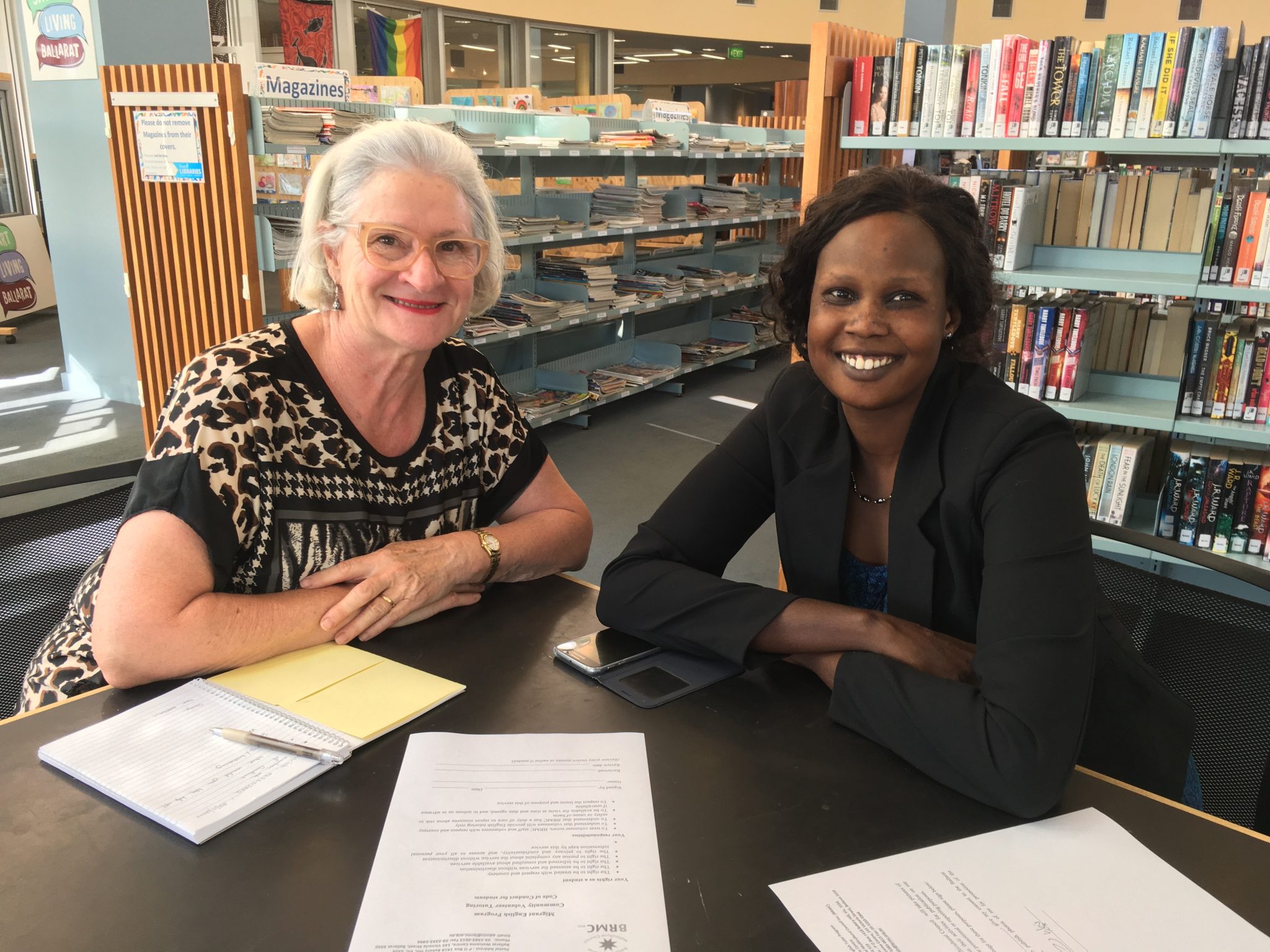 Two women smiling at library table.