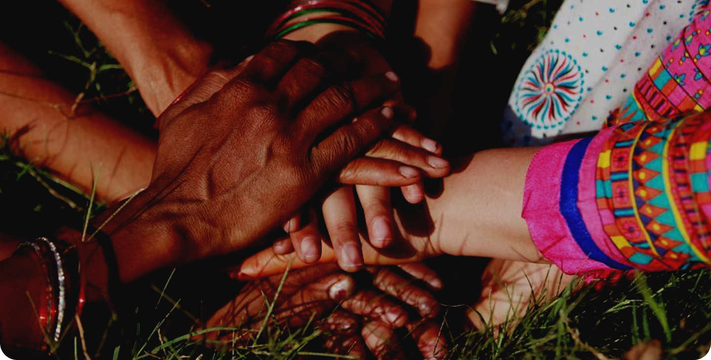Diverse hands stacked in unity on grass.