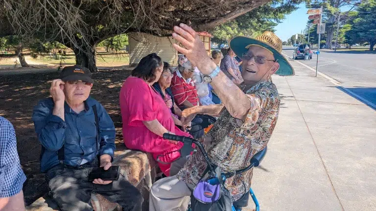 Elderly group sitting outdoors enjoying sunny day.