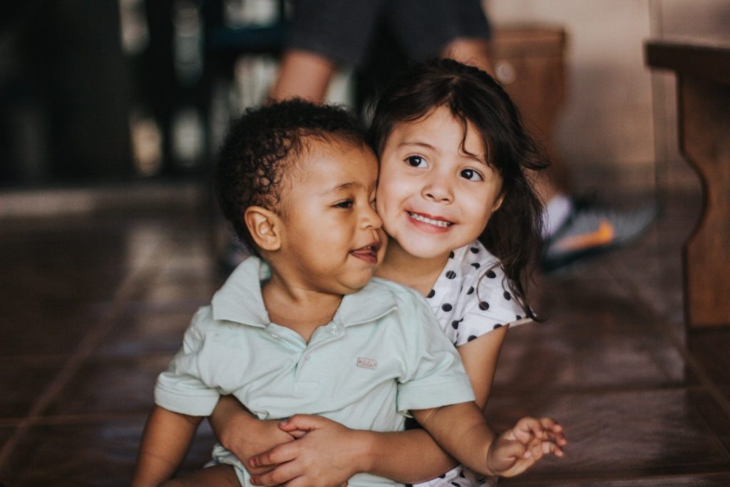 Two smiling children hugging on the floor.