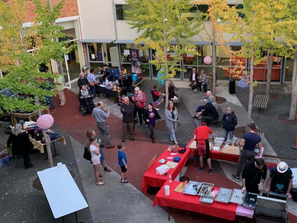 Community market with people mingling and food stalls.