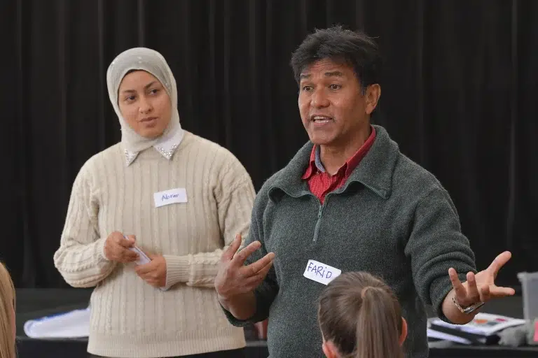 Two people speaking to a group indoors.