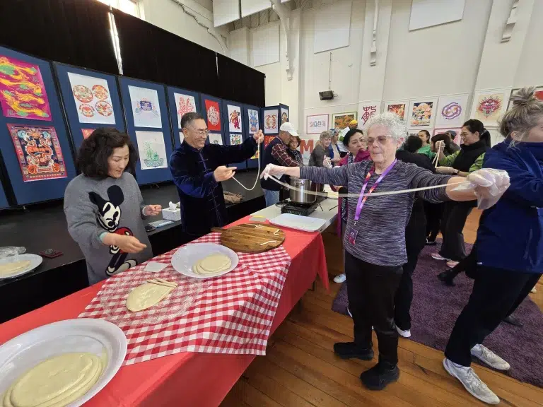 People making noodles at cultural event indoors.