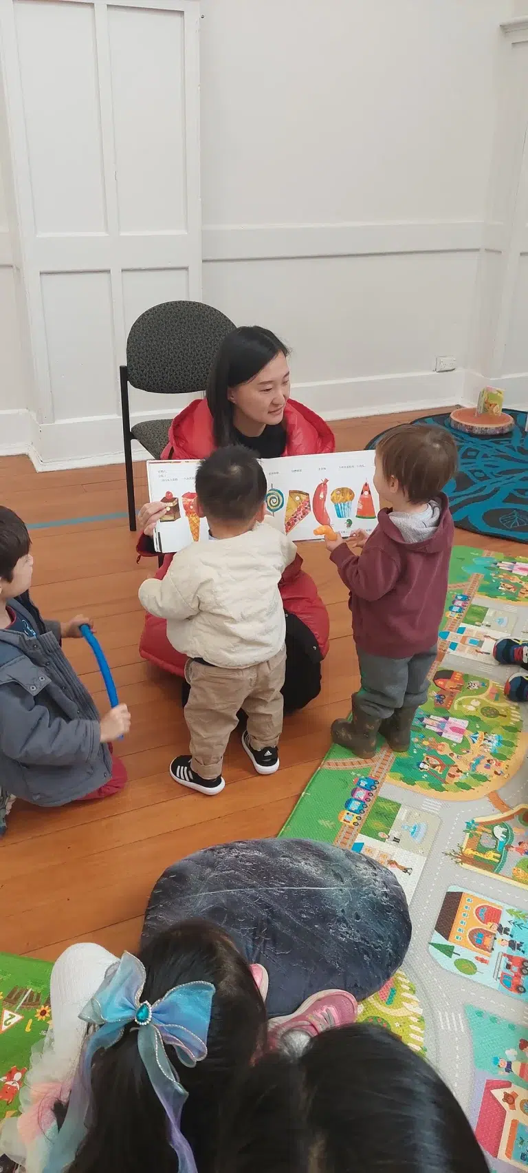 Storytime with teacher and kids on colourful mat.