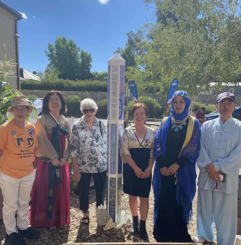 Diverse group standing around peace pole outdoors.