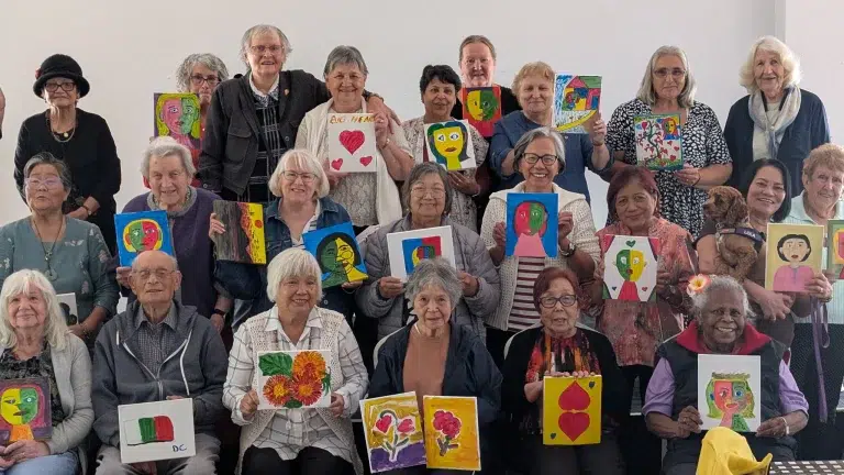 Group of seniors displaying colourful paintings together.