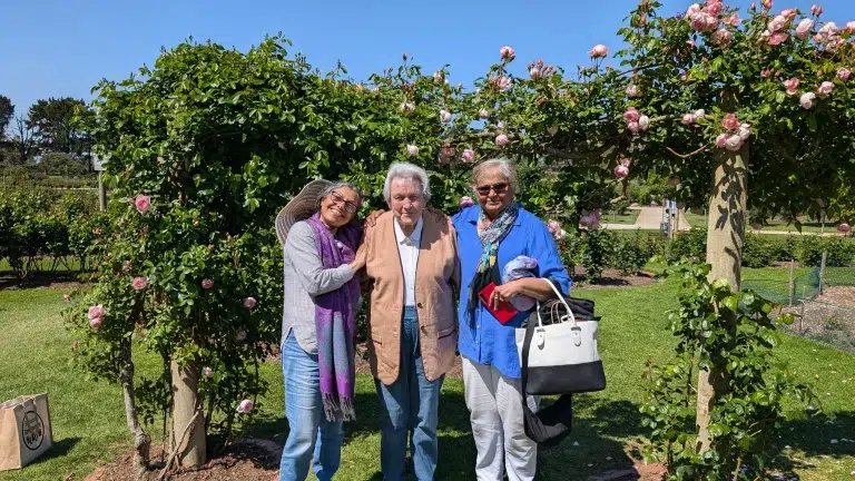 Three adults smiling in garden under rose arch.