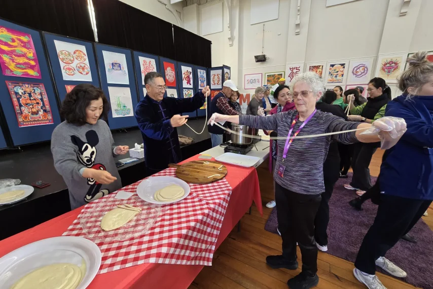 People making noodles at cultural event indoors.