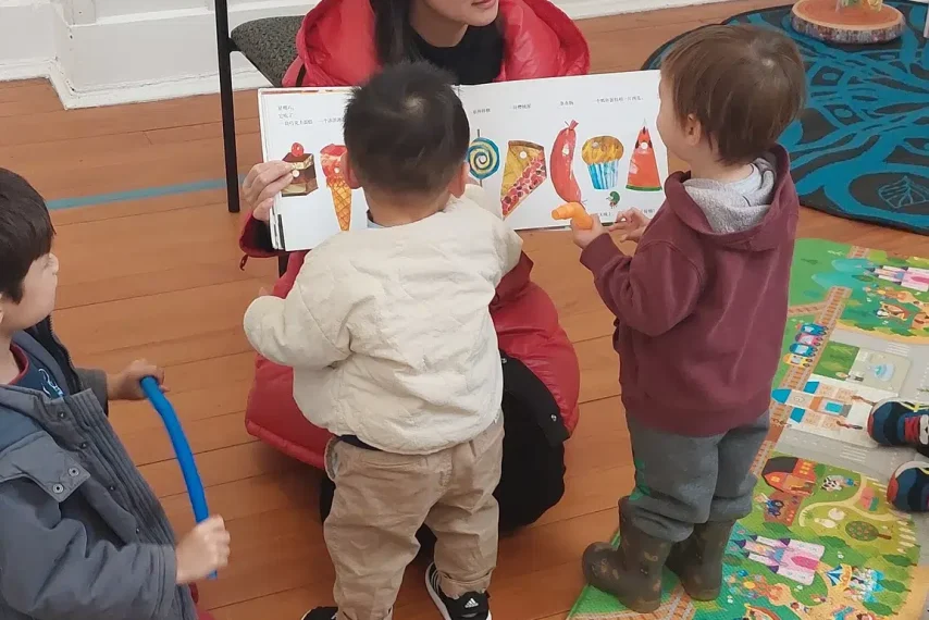 Storytime with teacher and kids on colourful mat.