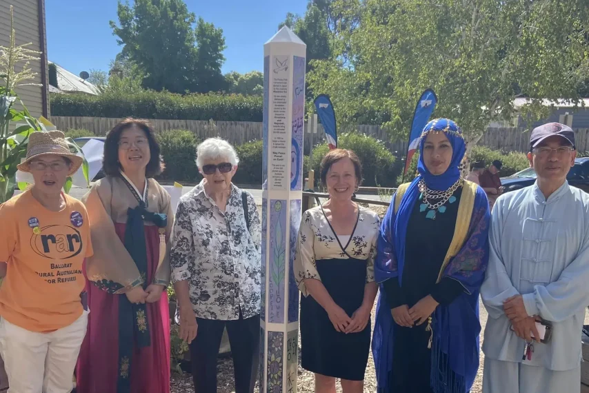 Diverse group standing around peace pole outdoors.