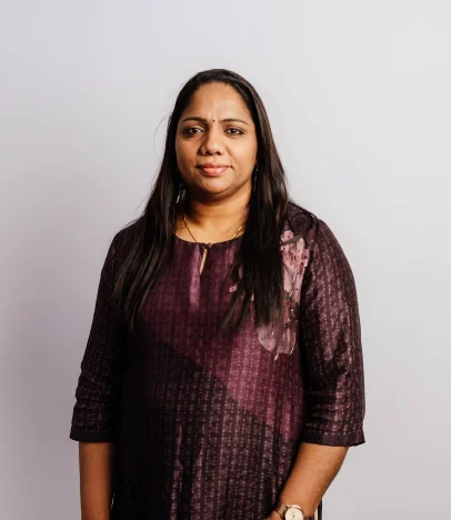 Woman wearing dark dress, standing against plain background.