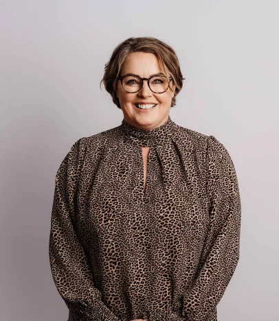 Smiling person wearing glasses and leopard print top.