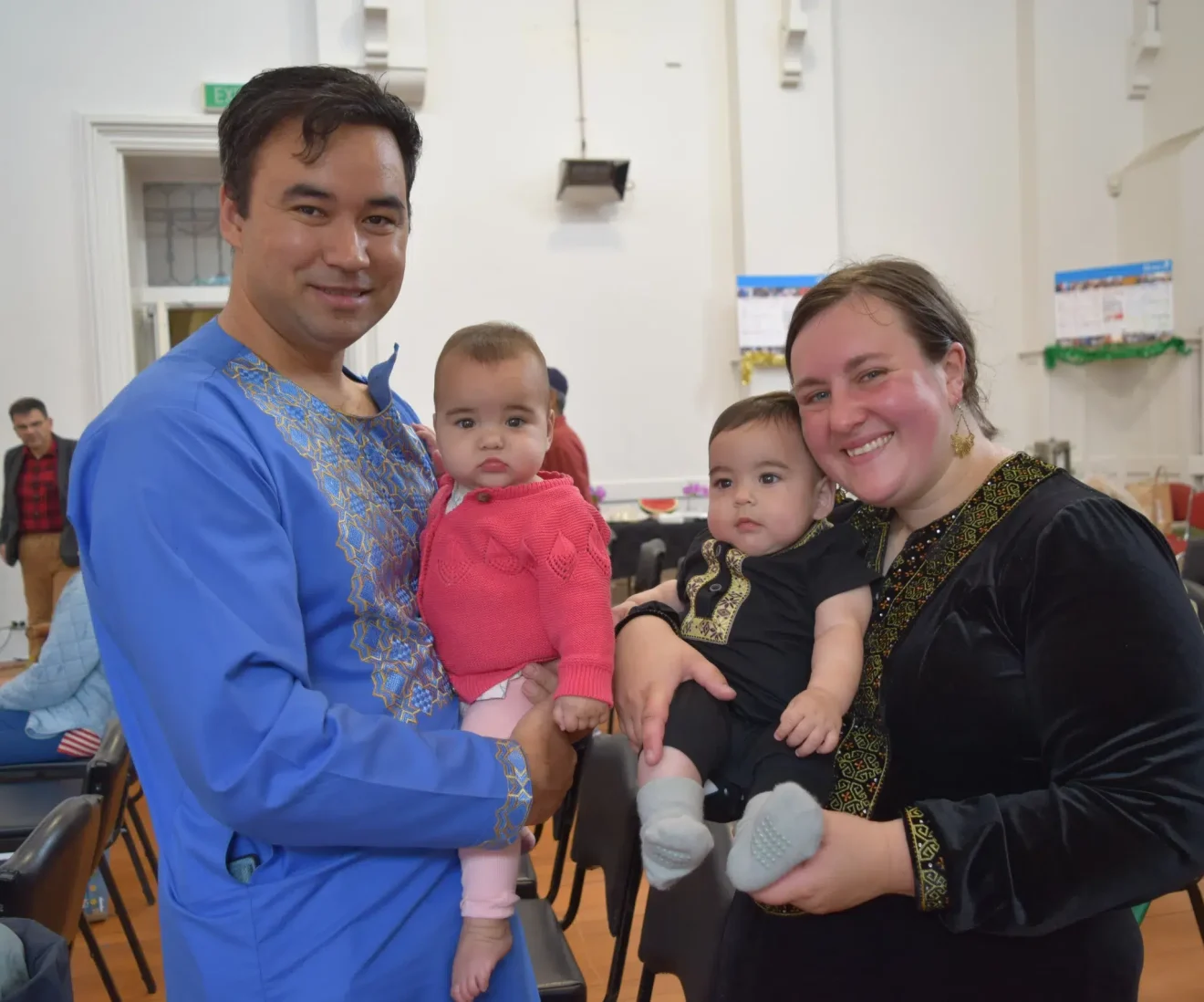 Family holding babies at cultural event indoors.