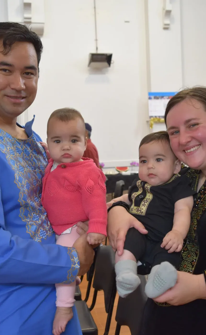 Family holding babies at cultural event indoors.