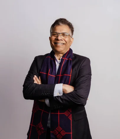 Smiling man in suit and scarf, arms crossed.