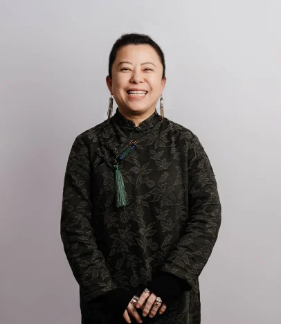 Smiling person in dark floral dress and earrings.