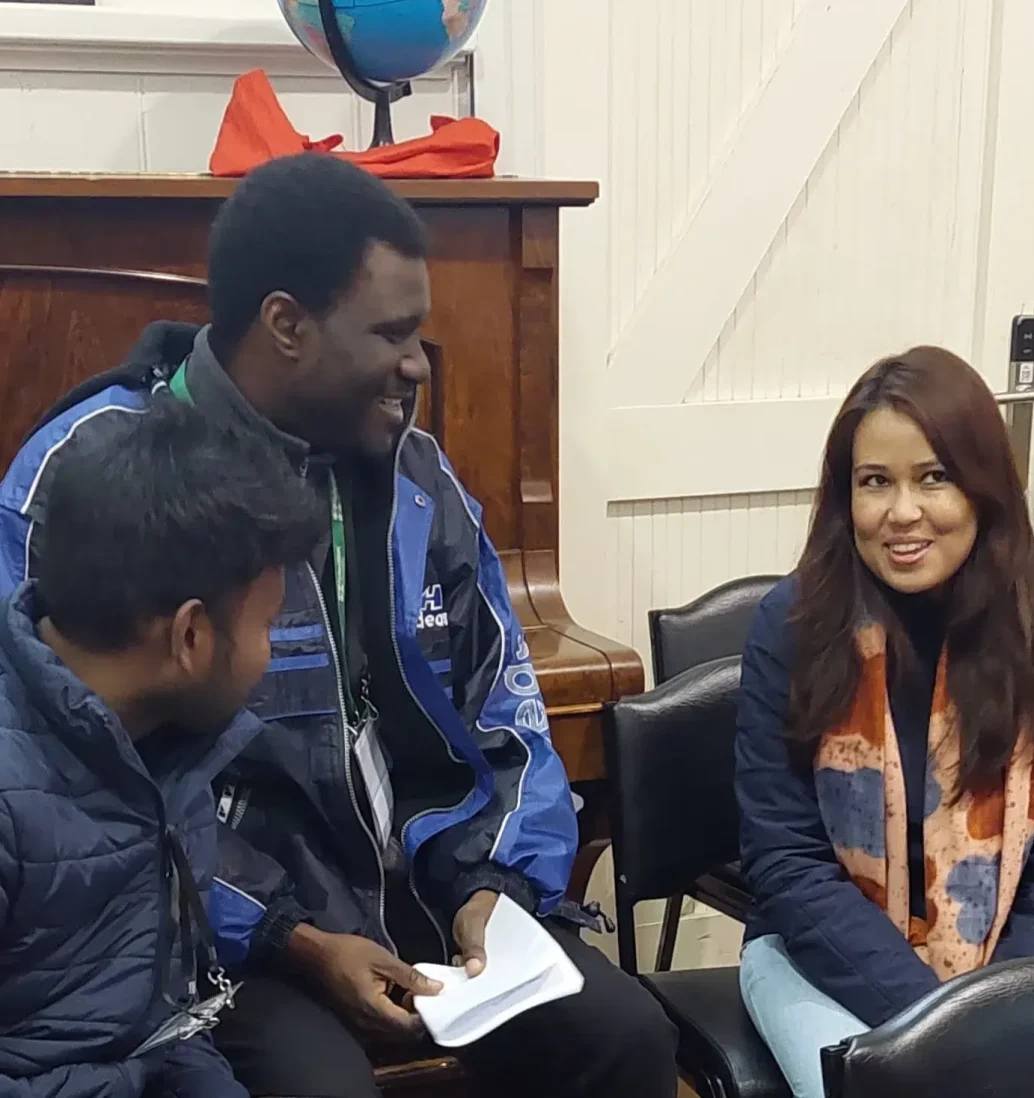 Three people chatting near piano with globe.