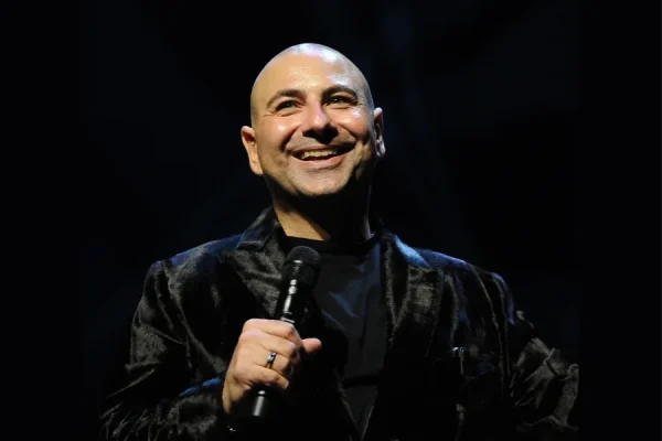 Man in black jacket holding microphone on stage.
