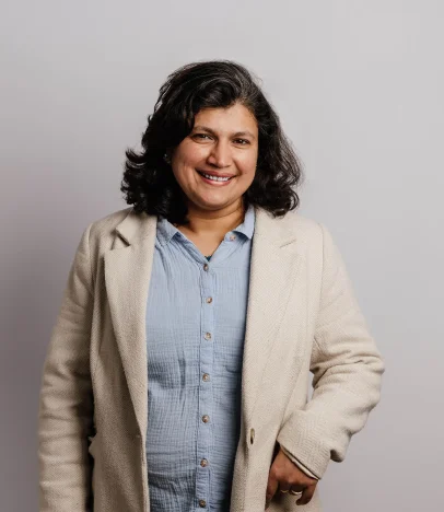 Smiling person in beige coat and blue shirt.