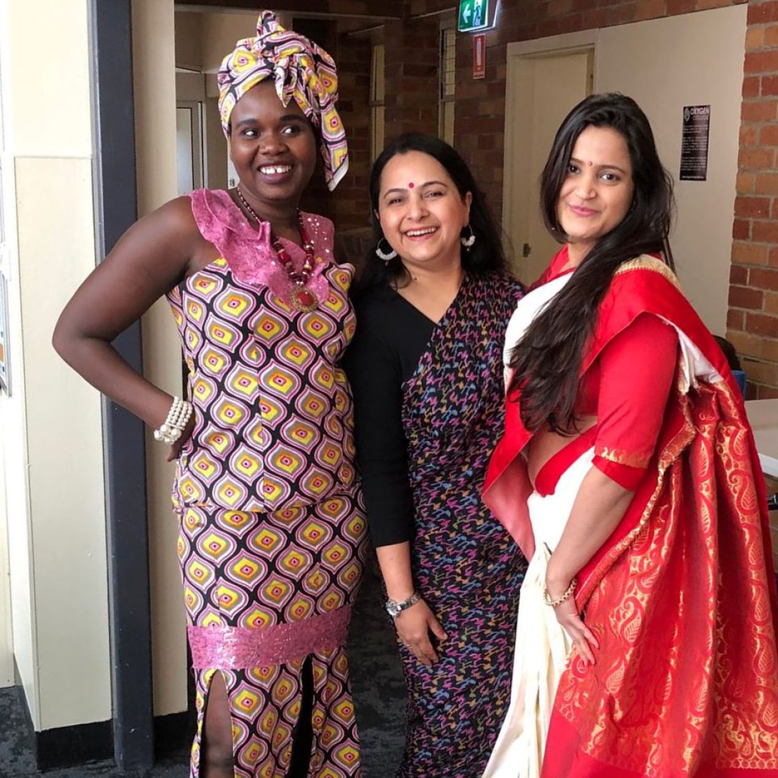 Three women in colourful cultural attire smiling together.