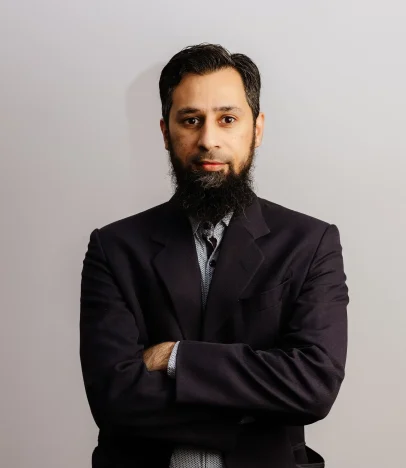 Man in suit with beard, arms crossed, confident.
