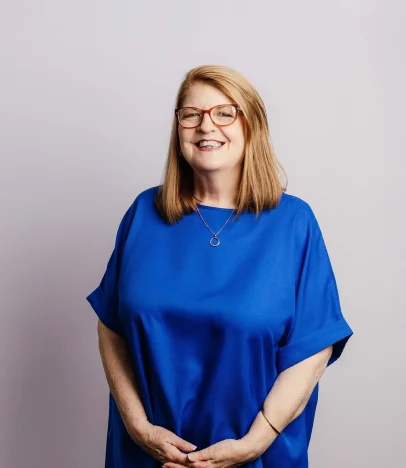 Smiling woman in blue shirt, glasses.