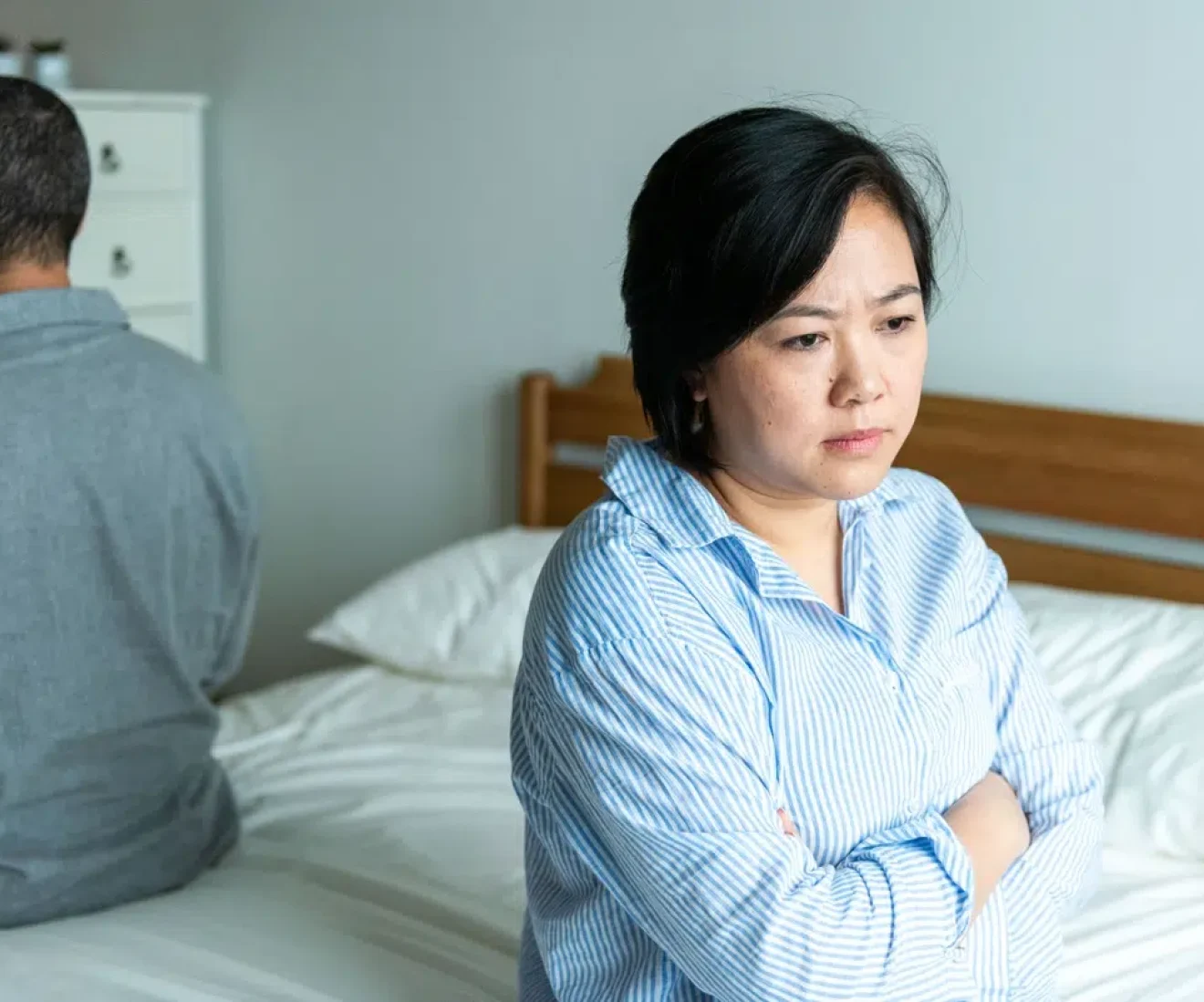 Upset couple sitting apart in bedroom.