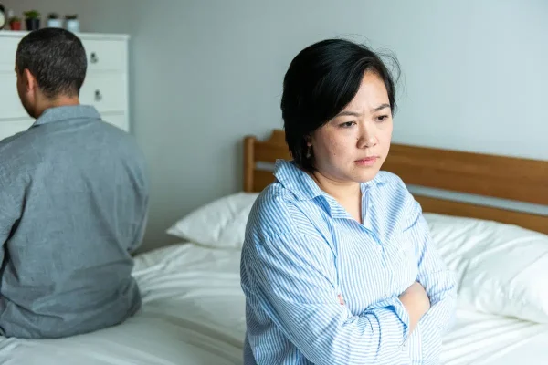 Upset couple sitting apart in bedroom.