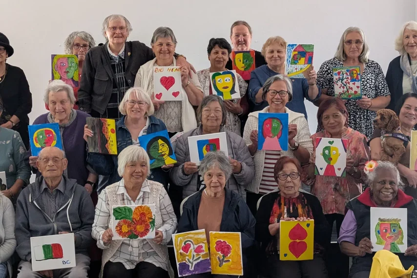 Group of seniors displaying colourful paintings together.