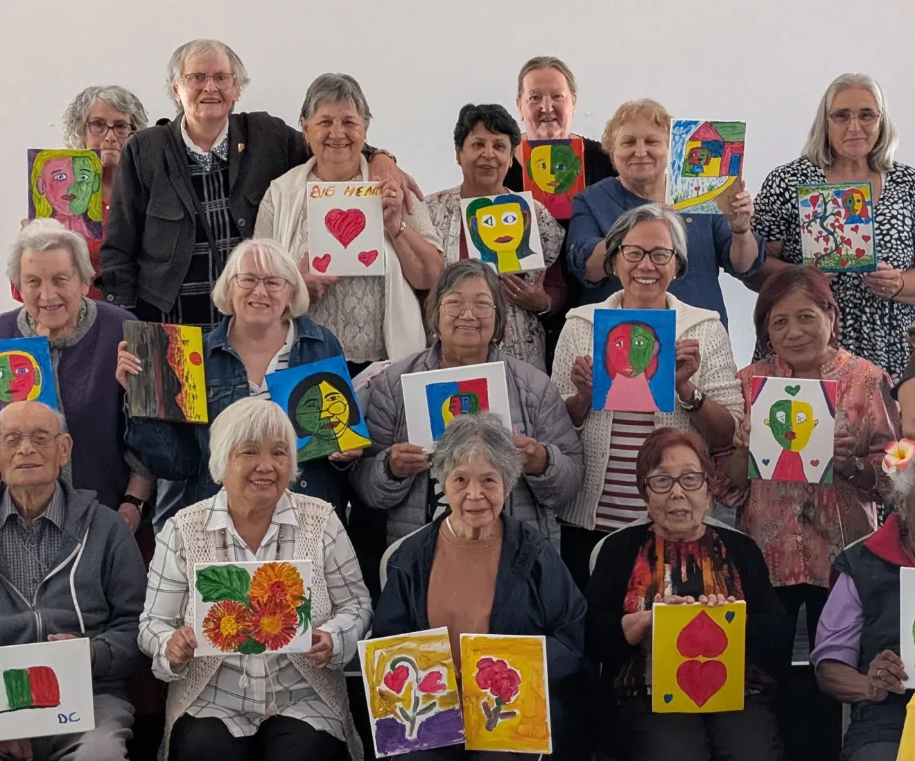 Group of seniors displaying colourful paintings together.