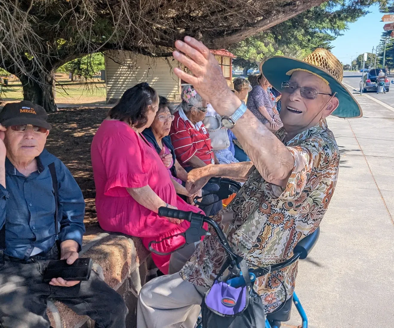 Elderly group sitting outdoors enjoying sunny day.