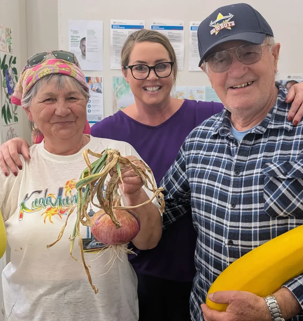 Smiling people holding large yellow zucchinis and onion.